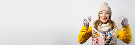 Young woman with smile holds a shopping bag with gifts on a light background. Concept of the winter...