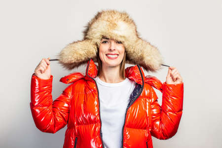 happy young girl in a red jacket and a fur hat on a light background. Concept fashion, shopping, good mood.の写真素材