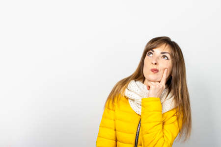 Woman in a jacket and a scarf with a surprised face looks up on a white background. Concept dream,...