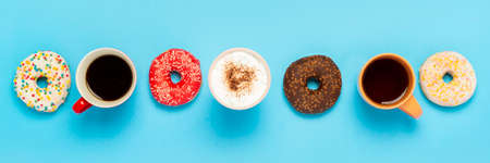 Tasty donuts and cups with hot drinks, coffee, cappuccino, tea on a blue background. Concept of sweets, bakery, pastries, coffee shop, meeting, friends, friendly team. Banner. Flat lay, top view.の写真素材
