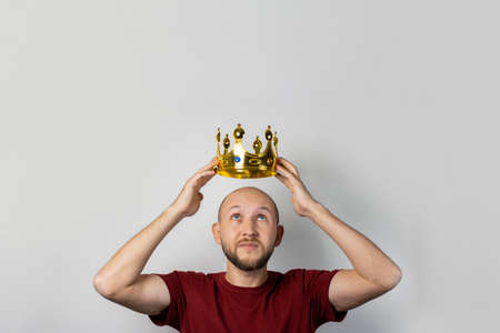 Young man tries on a golden crown on a light background. Concept is king, luck, gain, rich, dream, goal, aspiration. Banner.の写真素材