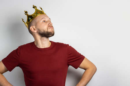 Young man tries on a golden crown on a light background. Concept is king, luck, gain, rich, dream,...