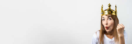 Young woman with a crown on her head emotionally rejoices and celebrates on a light background. Emotion laughter, surprise, shock. Concept of a queen, luck, victory, dream, goal, aspiration. Banner.の写真素材