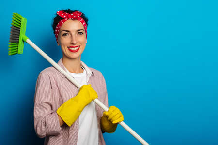 Smiling young woman in cleaning gloves holding a cleaning brush on blue background