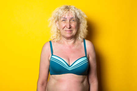 Smiling blonde old woman in swimsuit on bright yellow backgroundの写真素材