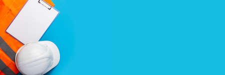 Construction hat, signal vest and blank sheet clipboard on light blue background. Concept for...