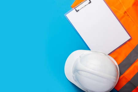 Construction hat, signal vest and blank sheet clipboard on light blue background. Concept for construction, renovation work. Banner. Flat lay, top view.の写真素材