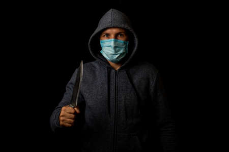 Young man in a medical mask holding a knife looking at the camera on a black backgroundの写真素材