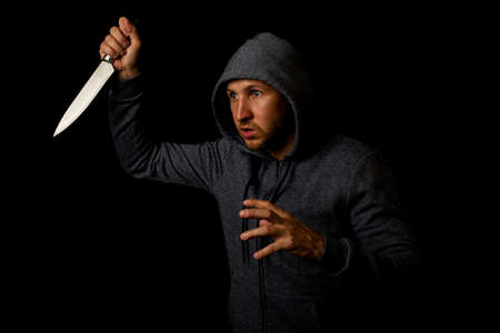 Aggressive young man in a sweatshirt in a hood with a knife on a black background