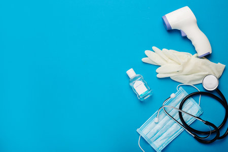 Digital non-contact thermometer, protective mask, latex gloves, medical stethoscope and sanitizer on a blue background. Banner. Top view, flat lay.の写真素材
