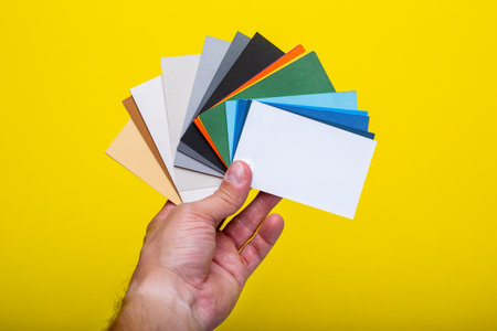 Hand holds a color palette of paints on a yellow background. Top view, flat lay. Banner.