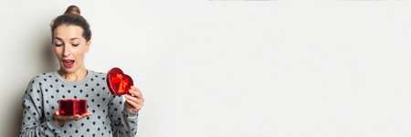 Surprised young woman rejoices with a gift on a light background. Valentine's day, birthday. Banner.