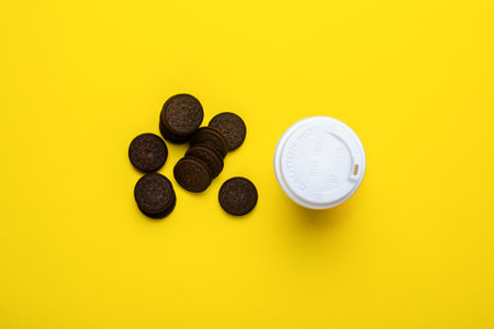 Cardboard cup with lid and chocolate chip cookies on a yellow background. Flat lay, top view
