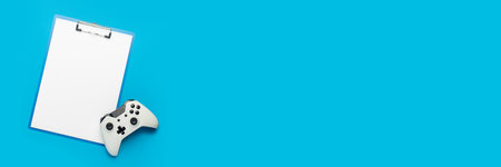 Clipboard with a blank sheet and a gamepad on a blue background. Banner. Flat lay, top view.