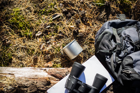 Tourist backpack, hat, binoculars and a map on a log in the forest. Concept of hiking, hiking in the mountains. Banner. Top view.の写真素材