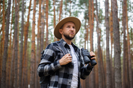 Man in a hat and a plaid shirt holds binoculars and walks through the forest.の写真素材