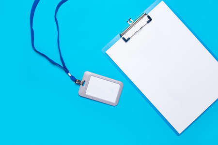 Blank clipboard and plastic name badge with blue drawstring on light blue background. Top view, flay layの写真素材