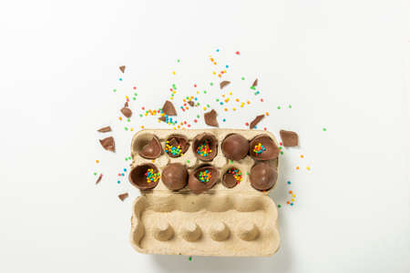 Tray with broken Easter chocolate eggs and multi-colored sweet candy decorations on a light background. Easter concept, easter treats, bunny. Banner. Flat lay, top view.の写真素材