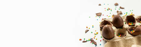 Tray with broken Easter chocolate eggs and multi-colored sweet candy decorations on a light...