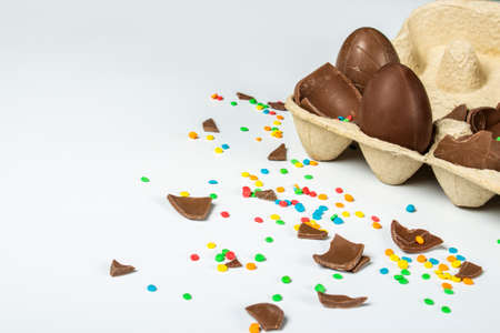 Tray with broken Easter chocolate eggs and multi-colored sweet candy decorations on a light background. Easter concept, easter treats, bunny. Banner.の写真素材