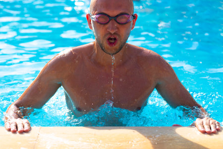 Man in swimming goggles training in blue water swimming pool.