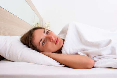 A young woman with open eyes is lying in bed. Concept insomnia, dreams, sleeping pills, problems.の写真素材
