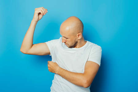 Young man in a white T-shirt with wet armpits from sweat on a blue background. Concept of excessive sweating, heat, deodorant.の写真素材