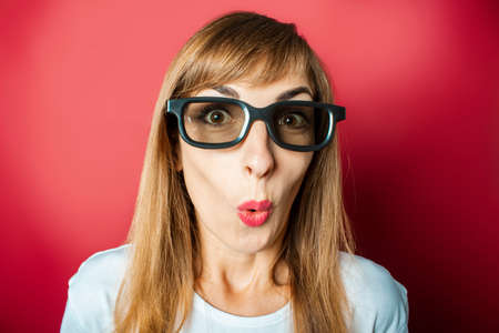 Young beautiful woman in glasses for watching movies and popcorn on a pink background. The concept of watching a movie, movie news, cinema, rating.の写真素材