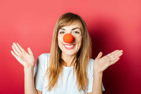 Young beautiful woman with a red nose of a clown on a pink background. Concept red nose day, holiday, party, clown.の写真素材