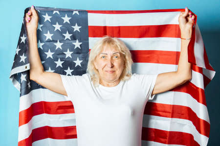 Old woman holds American flag on a blue background. Independence Day celebration concept, memorial day, emigration, US flag.の写真素材
