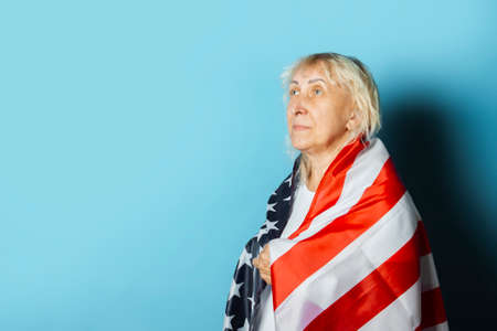 Old woman holds US flag on a blue background. Independence Day celebration concept, memorial day, emigration.の写真素材
