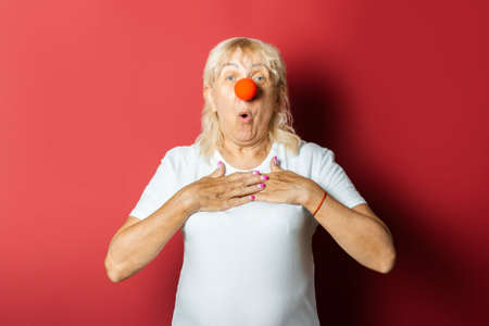 Funny old woman with a red nose of a clown on a pink background. Concept red nose day, holiday, party, clown.の写真素材