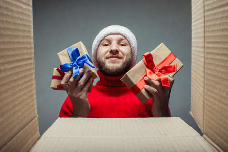 Man in a Santa Claus hat and a red sweater lays down, takes gifts in or out of the box. Concept of...