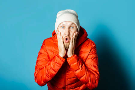 Man with a surprised face in a hat and a red jacket on a blue background. Concept surprise, shock.の写真素材