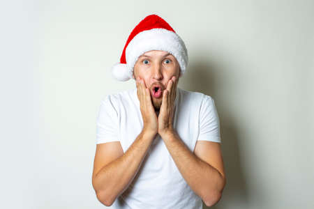 Young man with a surprised face in a hat of Santa Claus on a white background. Christmas concept sale, holiday.の写真素材