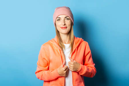 Beautiful Young woman in a hoodie and hat on a blue background. Concept of winter, christmas, winter holidays, the onset of cold weather.の写真素材