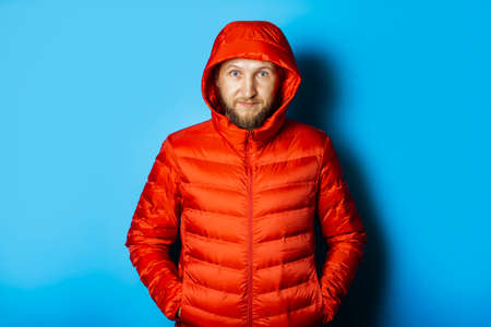 Man in a red jacket with a hood on a blue background. The concept of winter, autumn, cold.の写真素材