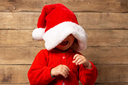 Little child in Santa Claus hat on wooden background. Christmas concept, family holidays.の写真素材
