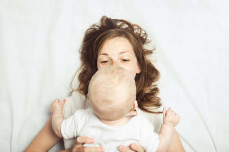 Young mother and the little baby on the bed with white sheets. Concept of education and child...
