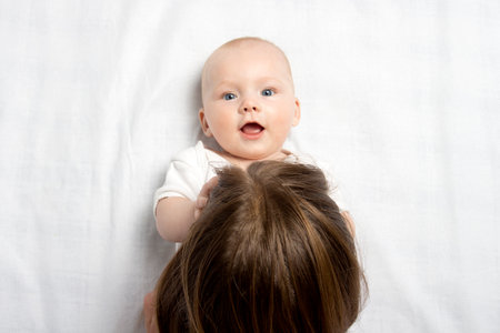 Little baby in white clothes and mom kisses him in the stomach on a white background. Flat lay, top...