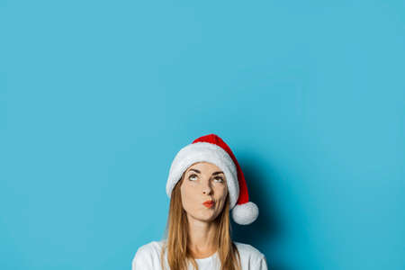 Young woman in Santa Claus hat with a mysterious face on a blue background. Concept idea for new year and christmas.の写真素材