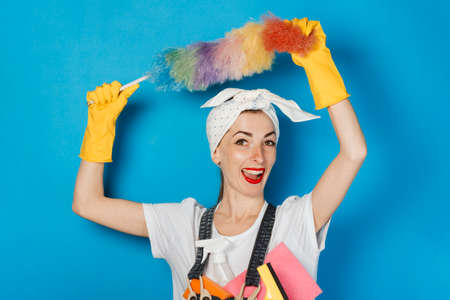 Young girl with a scarf on her head, yellow rubber gloves holds in her hands the means for cleaning and cleaning on a blue background. Concept of cleaning and cleaning service, high qualityの写真素材