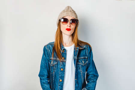 The girl in a denim jacket, glasses and hat on a white backgroundの写真素材