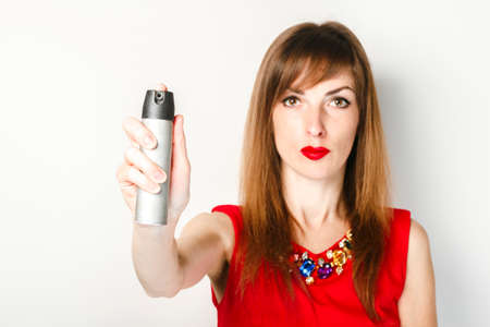 Young girl in a red dress holds a gas spray in her hand for protection against a light background....