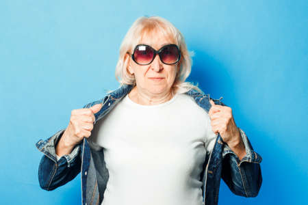 Old lady in a denim jacket and sunglasses on a blue backgroundの写真素材