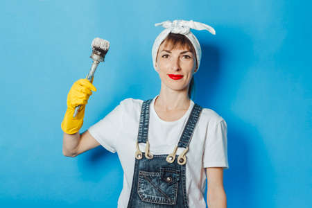 A young girl holding a brush with paint on a blue background. Painting concept, repair, building.の写真素材