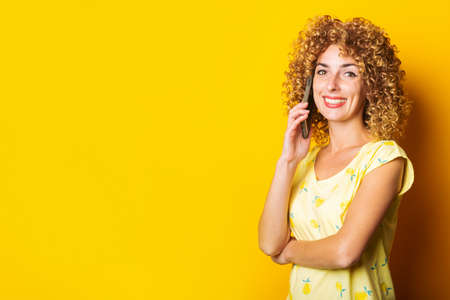 curly young woman smiling talking on the phone on a yellow background