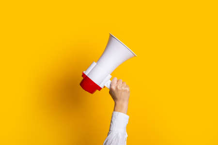 female hand holds a white with a red megaphone on a yellow backgroundの写真素材