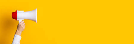 female hand holds a white with a red megaphone on a yellow background. Banner.