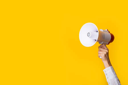 female hand holds a white with a red megaphone on a yellow background